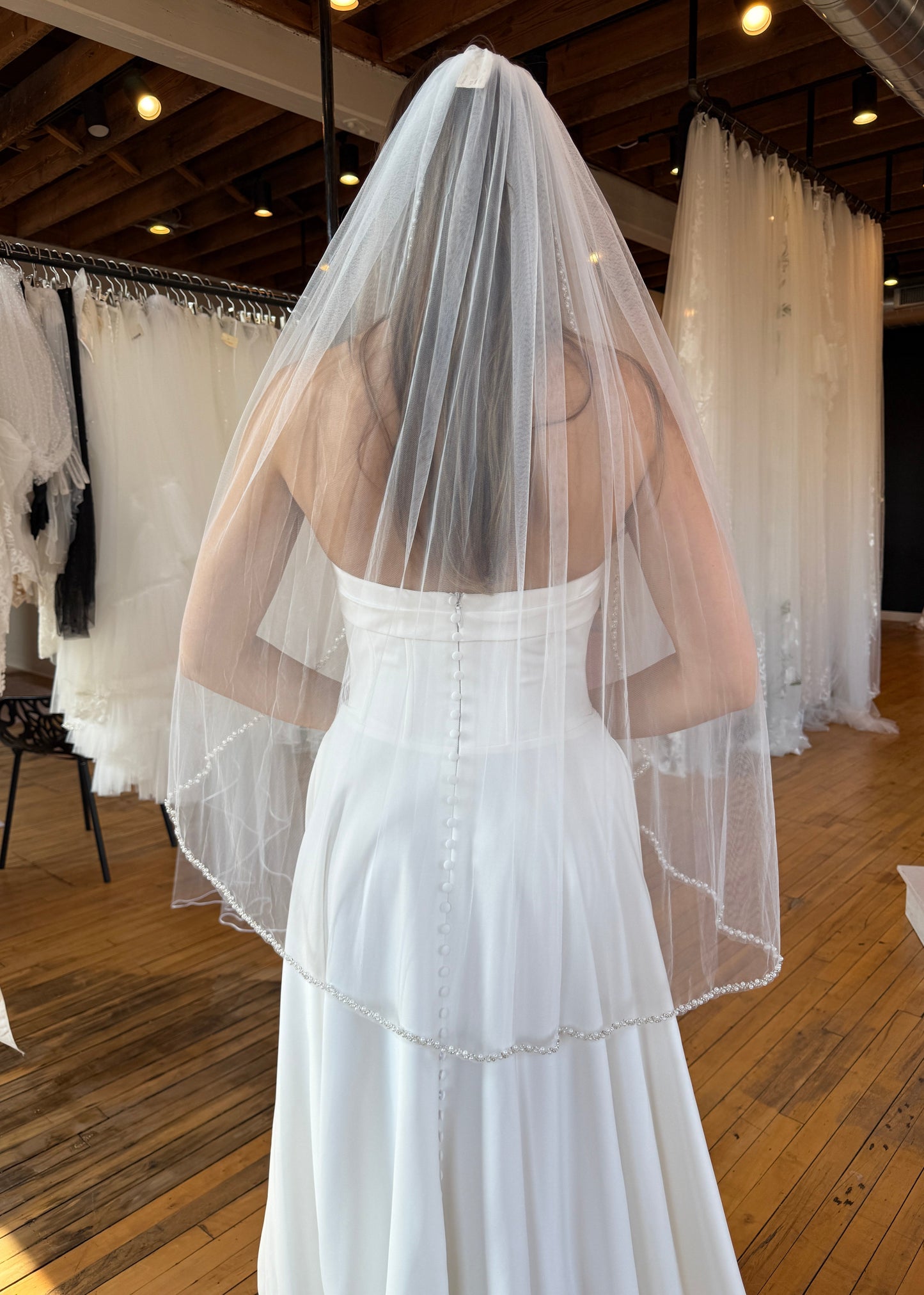 White wedding dress with sheer overlay on a wooden floor.