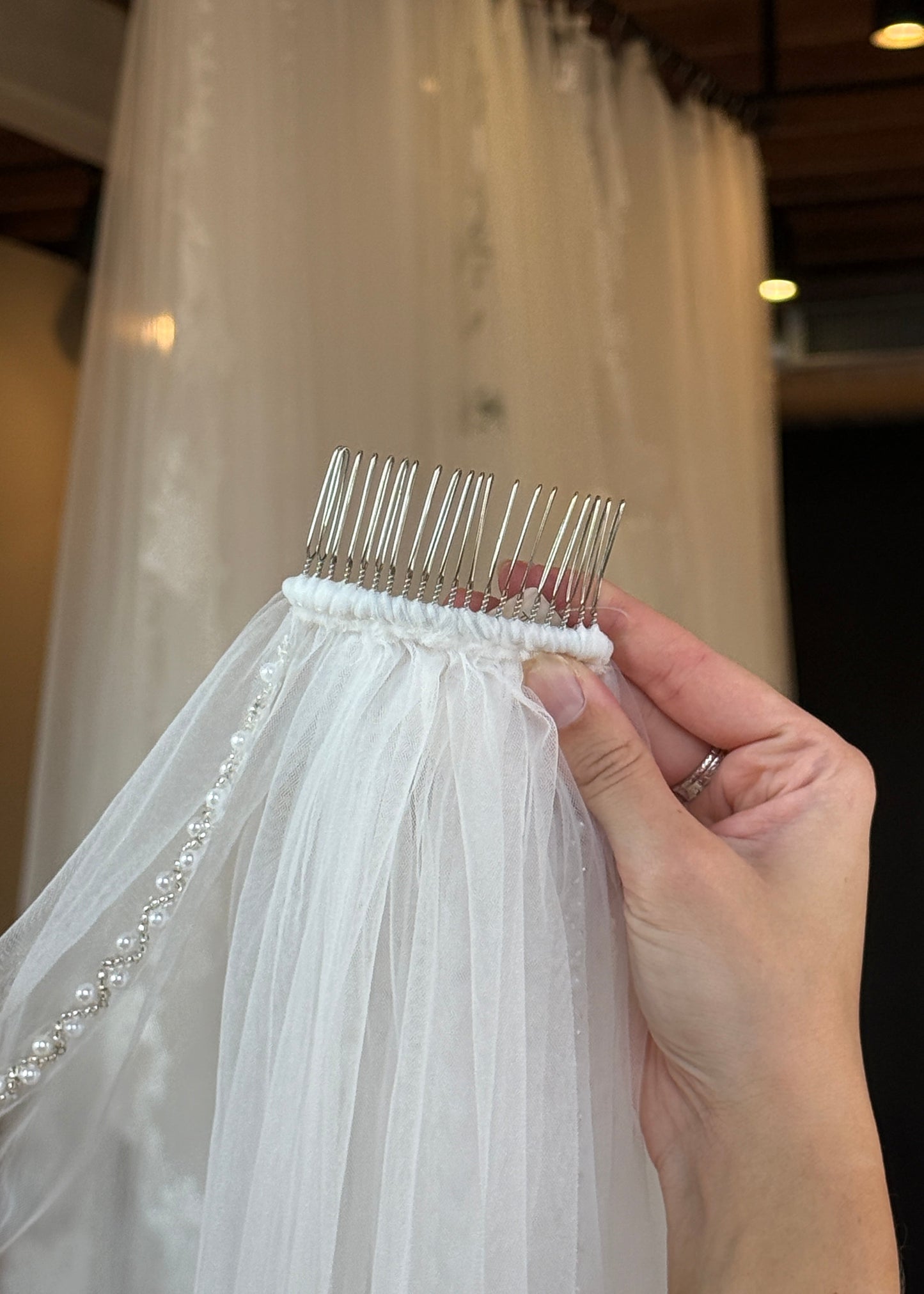 Close-up of a hand holding a section of a white wedding dress with beaded trim.