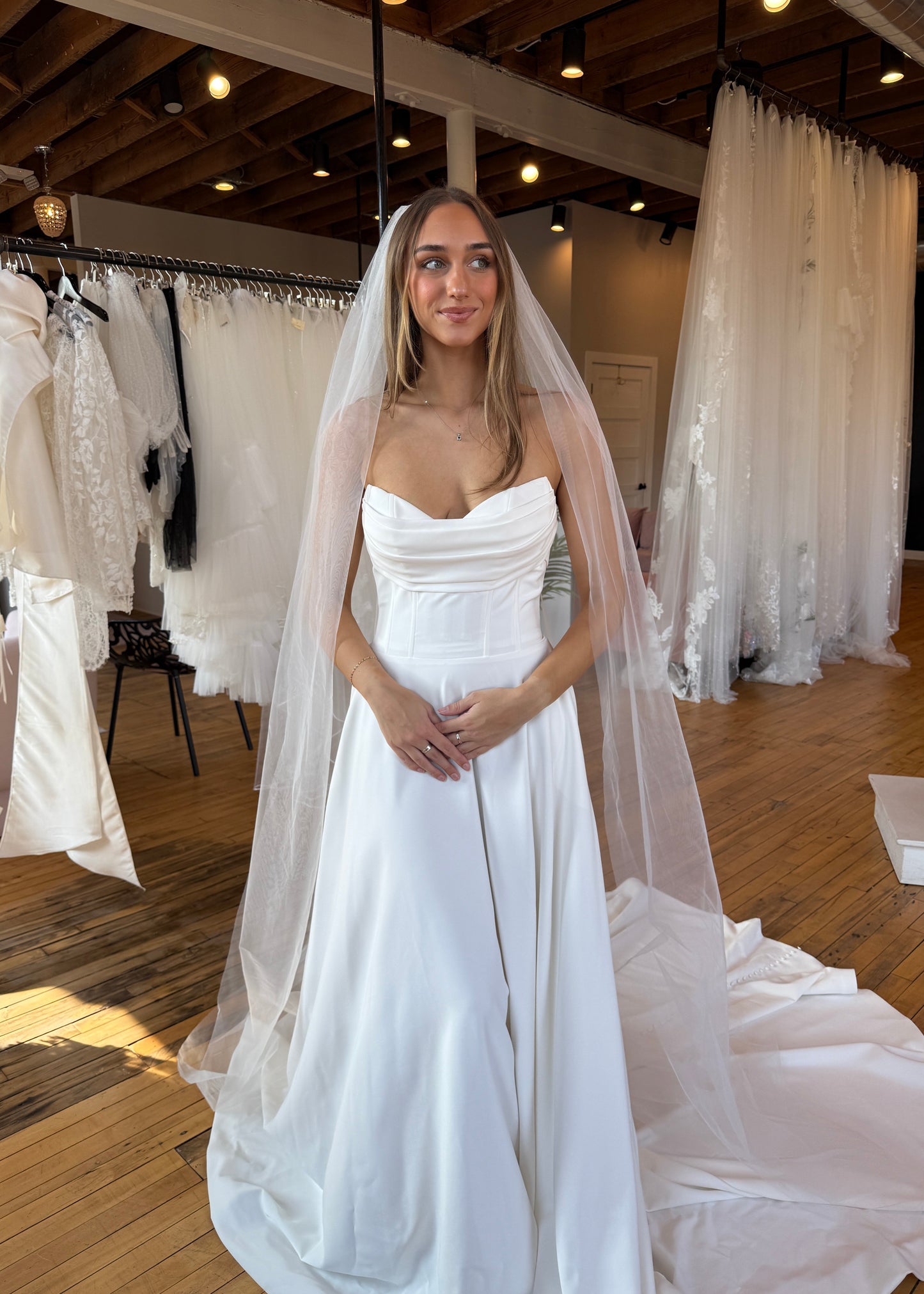 Woman trying on a white wedding dress with multiple veils in the background.