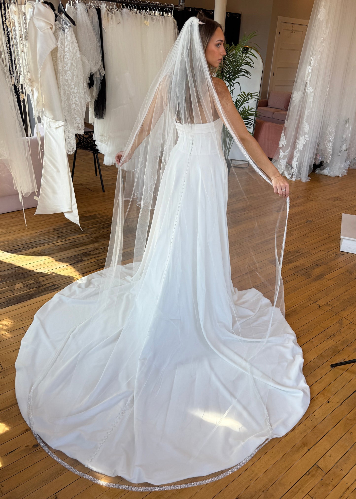 White wedding dress with a long train being held up on a wooden floor.