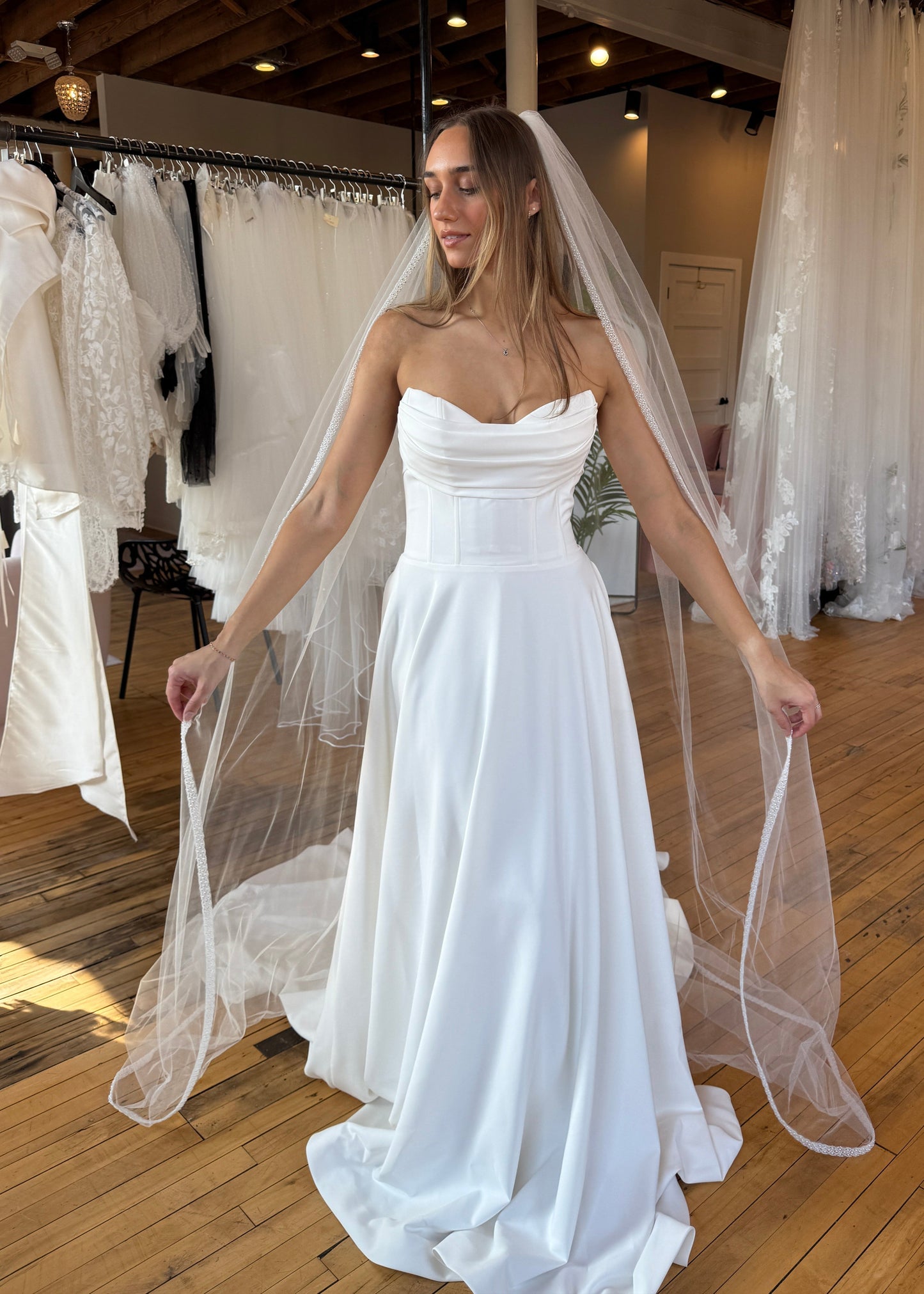 Woman holding a white wedding dress with a long train in a store setting.