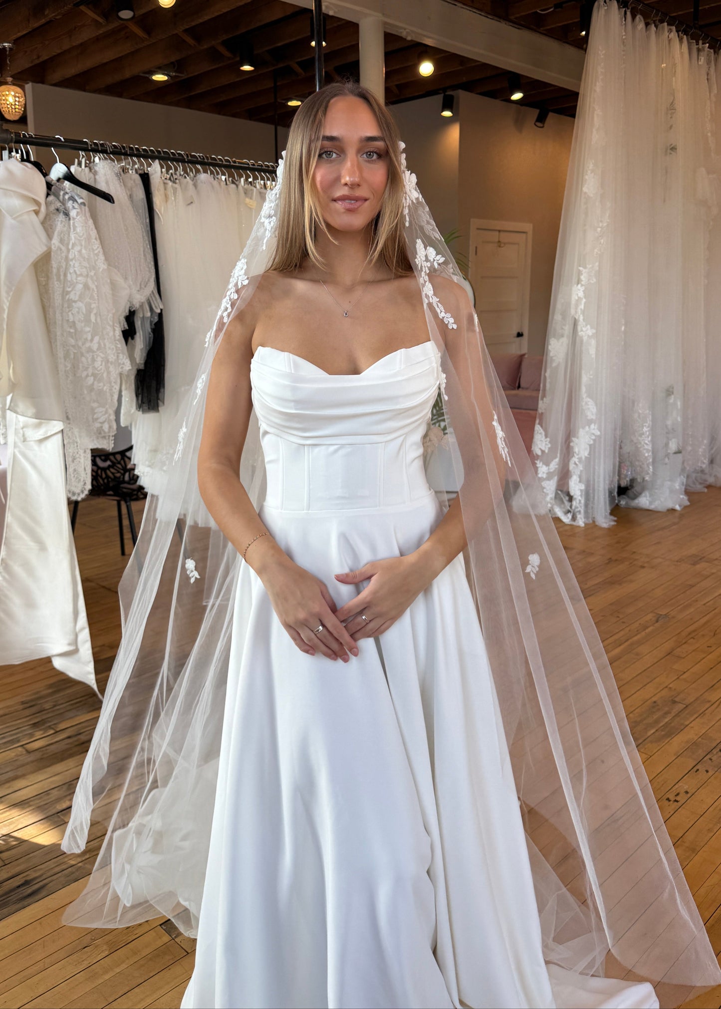 Woman holding a white wedding dress with a long train in a store setting.