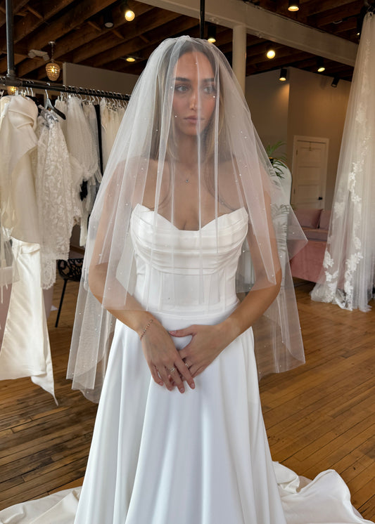 Woman wearing a white wedding dress with a veil in a bridal shop.