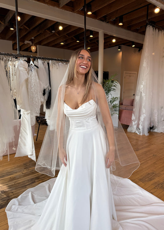 Woman trying on a white wedding dress in a store with multiple dresses displayed.